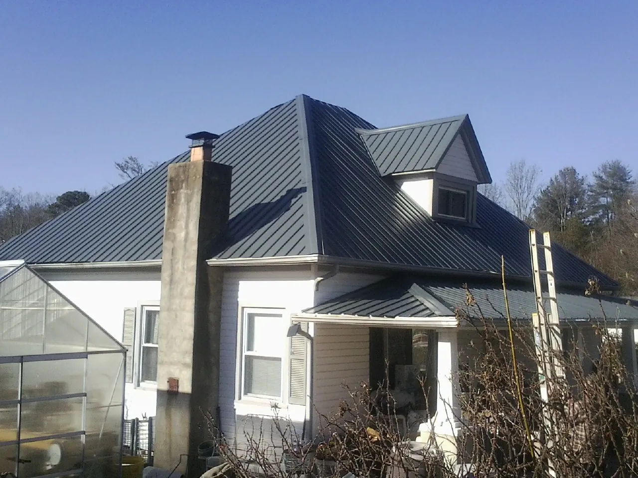 Dark blue standing seam metal roof on a white farmhouse with dormer — Slate & Tile Roof Repair by Roofing Brothers in Portersville