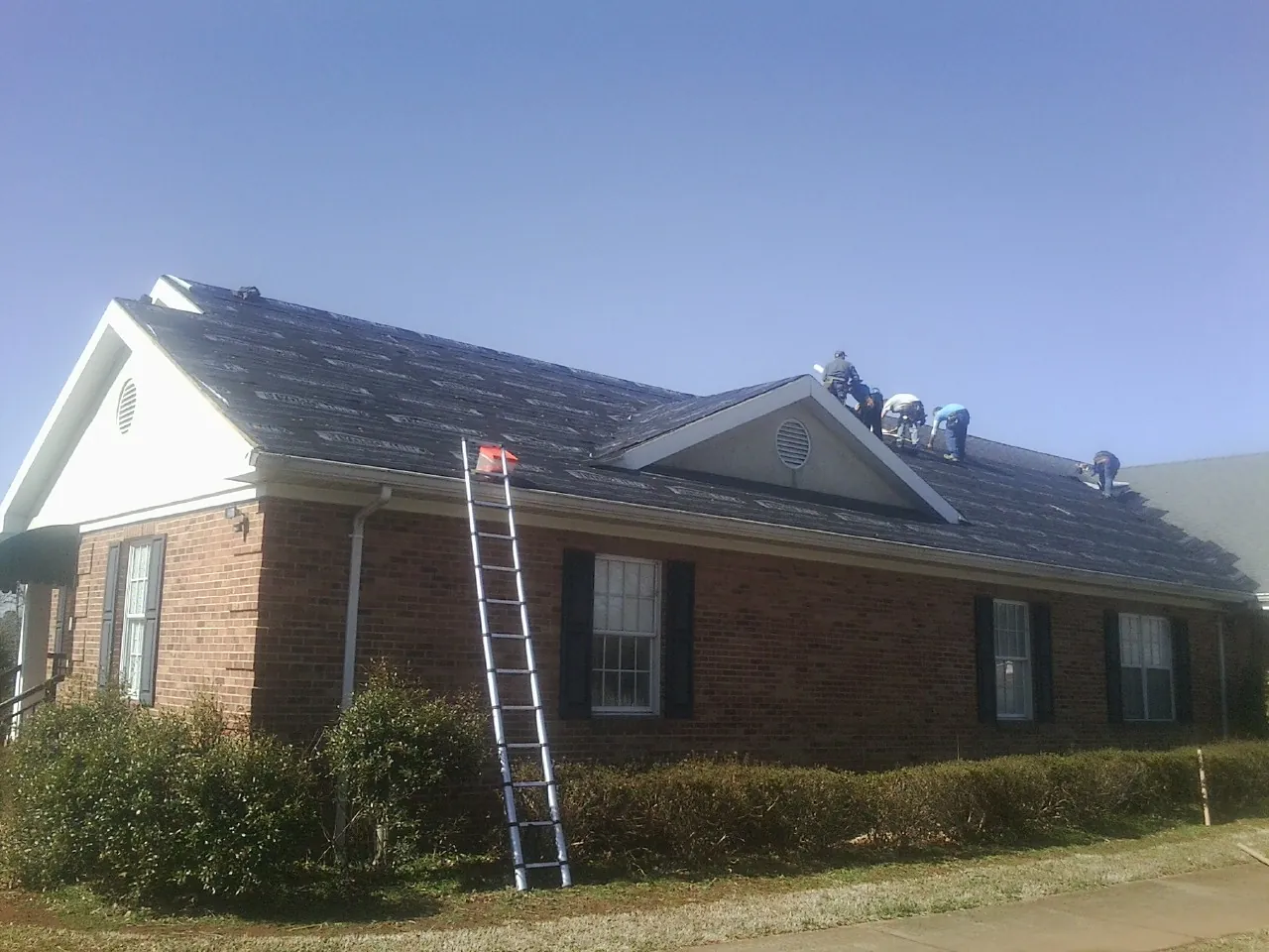 Crew tearing shingles off a brick ranch roof with a ladder set — Metal Roof Repair work by our crew in Portersville