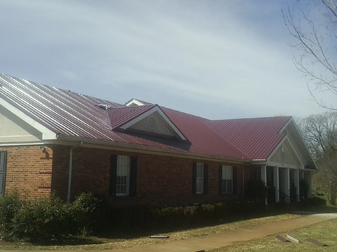 Red metal roof with gabled entries on a long brick building, from a Hail Damage Roof Repair job in Portersville