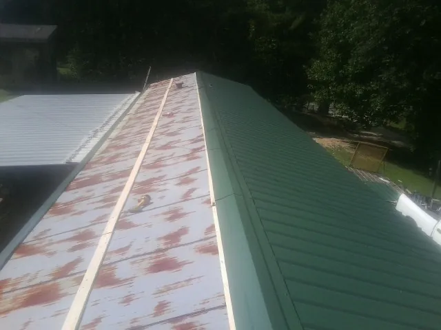 Old rusted panels beside newly installed green metal roofing — Wind Damage Roof Repair by Roofing Brothers in Portersville