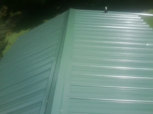 New green metal panels meeting at the ridge of a roof — Flat Roof Repair work by our crew in Portersville