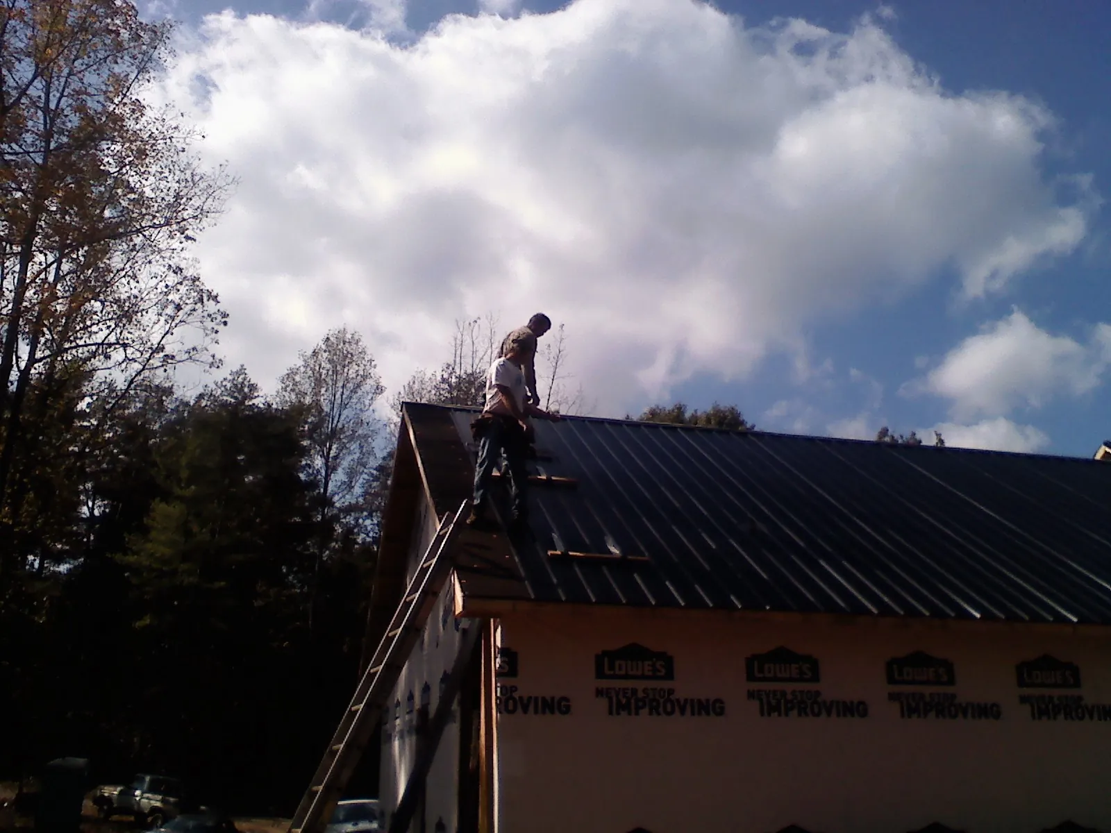 Roofer fastening dark metal panels high against a cloudy sky, from a Roof Inspection job in Portersville