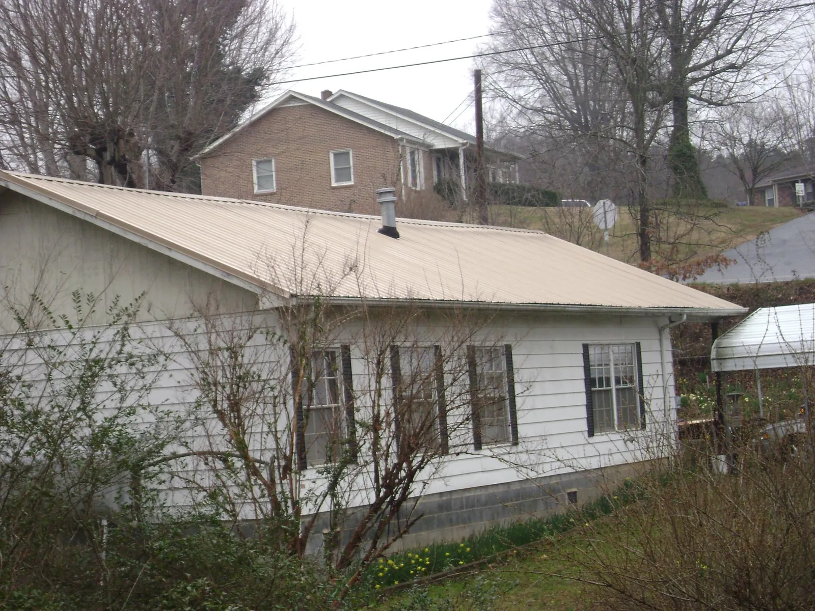 Tan metal roof on a white sided house set into a hillside — Commercial Roofing by Roofing Brothers in Portersville