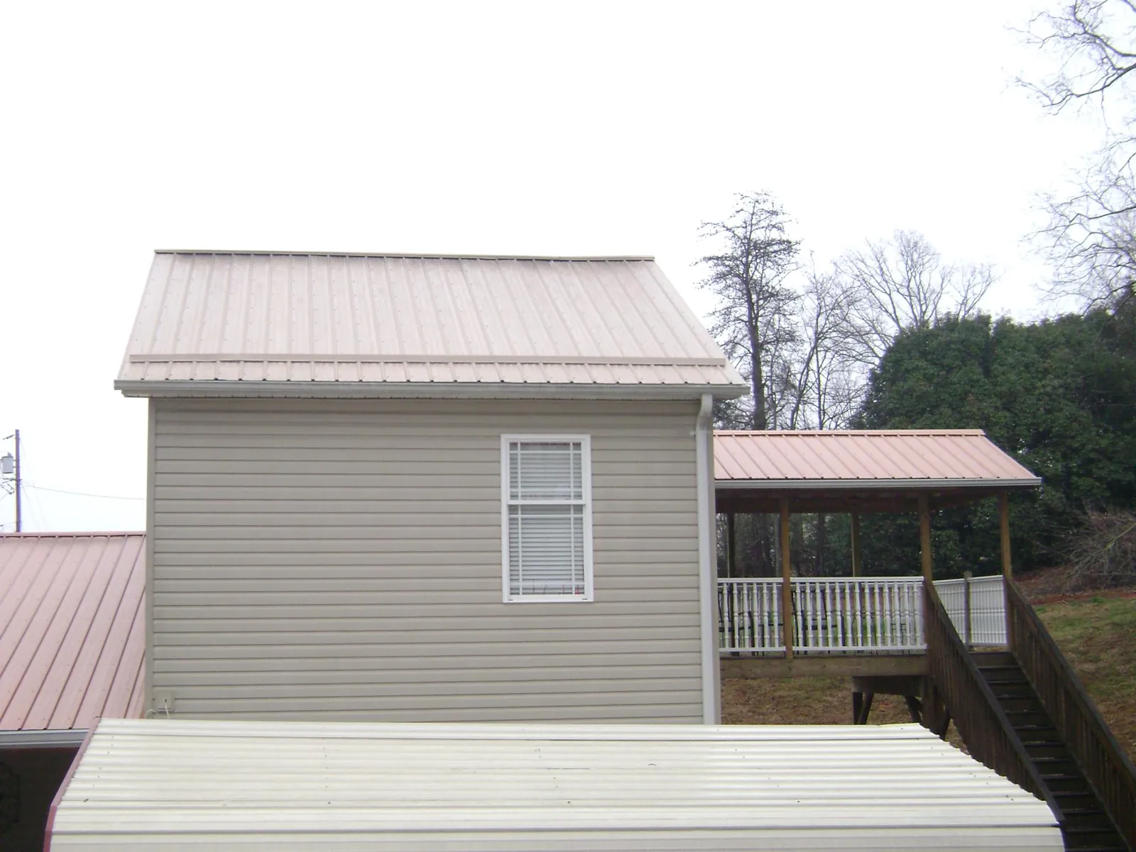 Tan metal roofs on a two story addition and attached porch, from a Roof Replacement job in Portersville